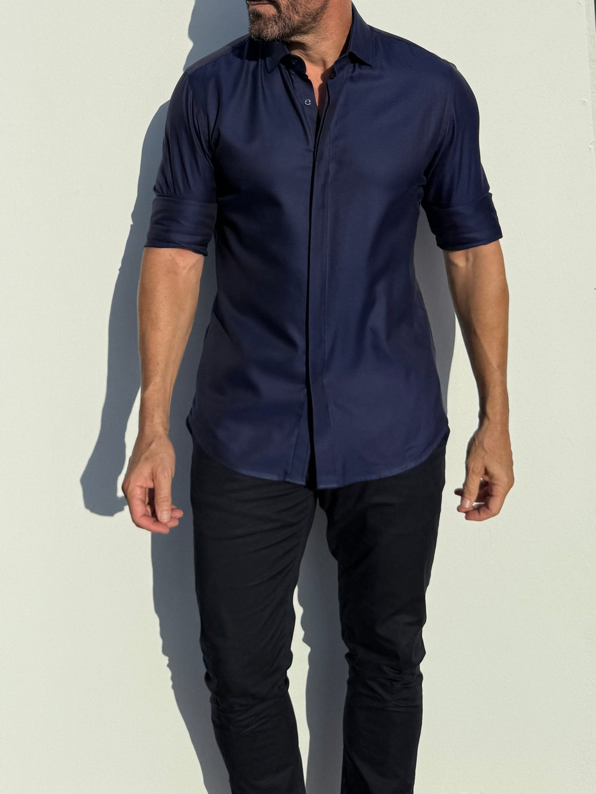Man wearing a navy blue shirt and black pants against a light background