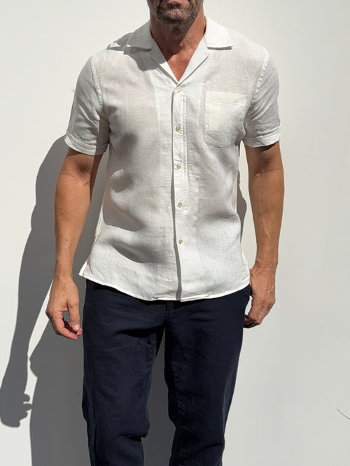 Man wearing a white short-sleeve shirt and dark pants against a light background