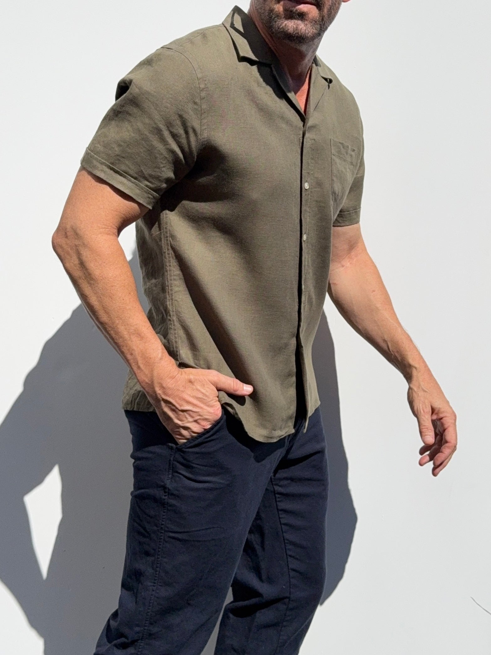 Man wearing a green shirt and dark pants against a white background