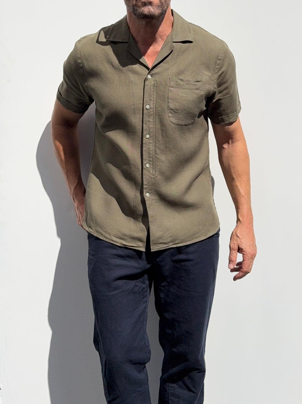 Man wearing a green button-up shirt and dark pants against a white background