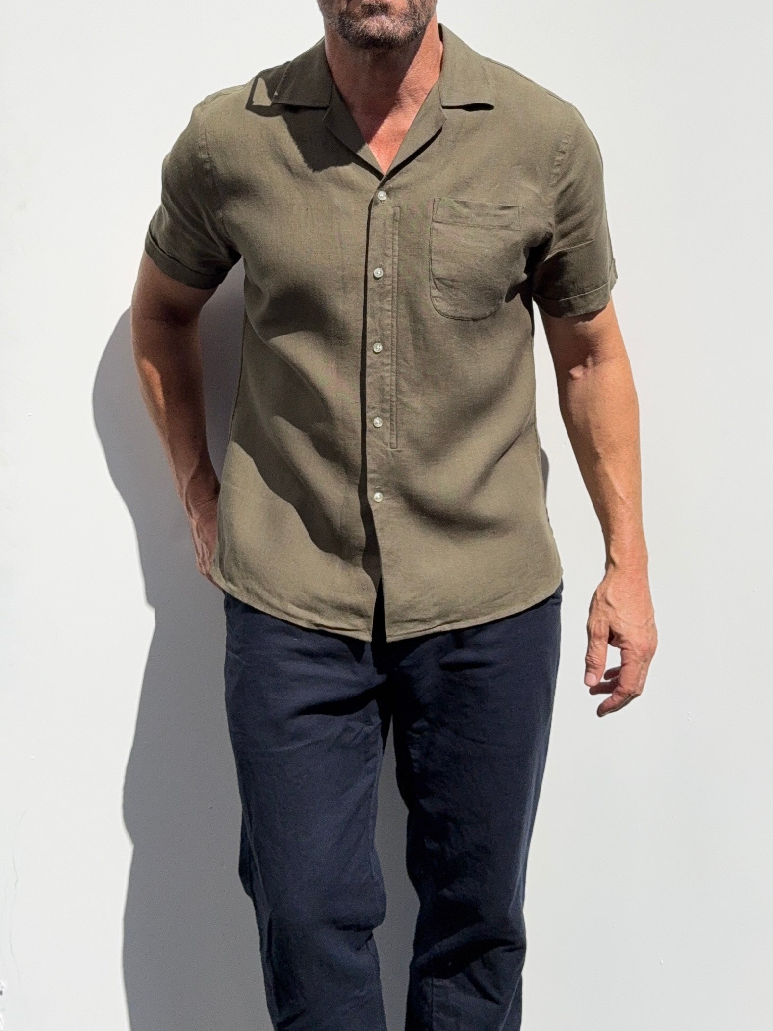 Man wearing a green button-up shirt and dark pants against a white background
