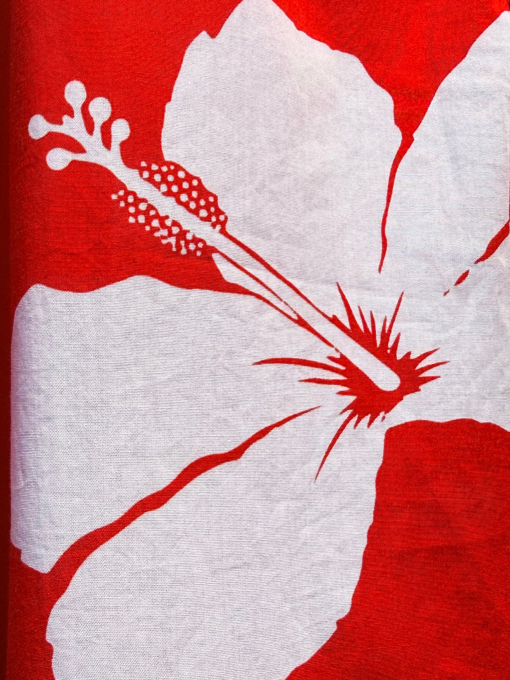 Close-up of a red Hawaiian-style shirt with a large white hibiscus flower print and a zipper detail.