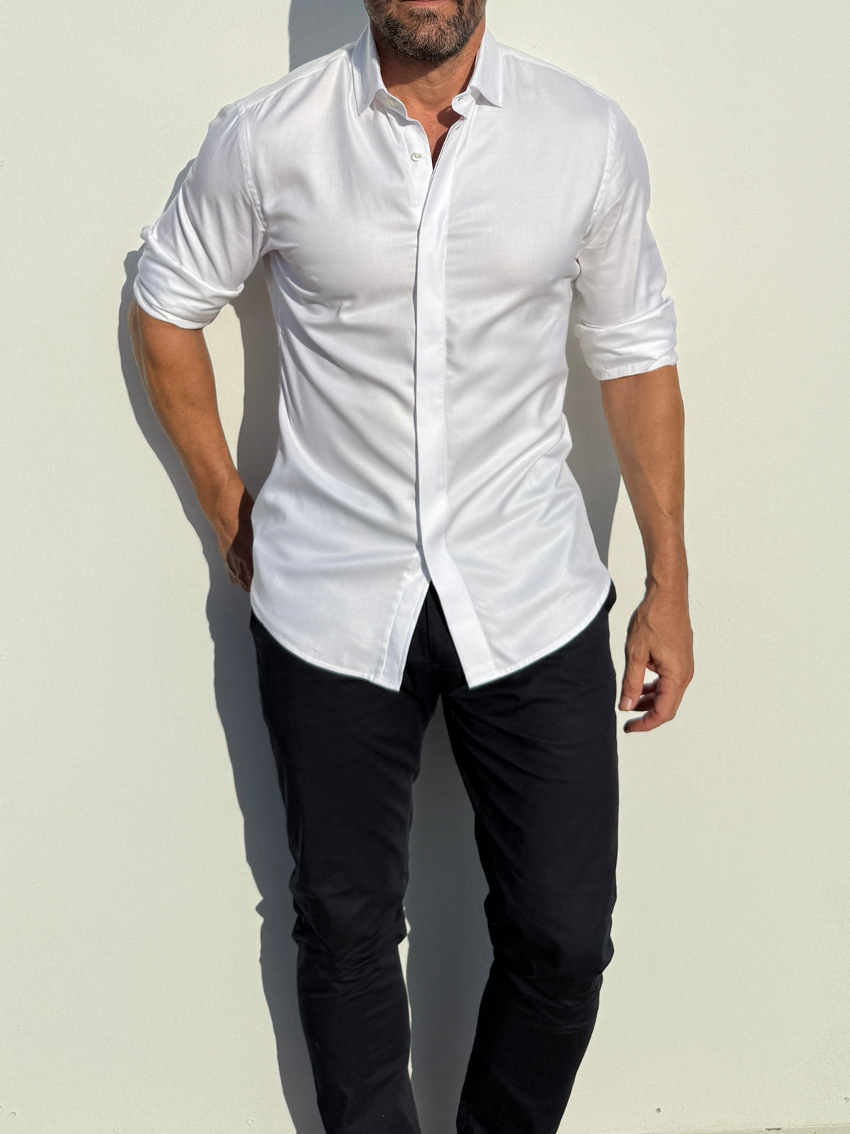 Man wearing a white button-up shirt and black pants against a light background