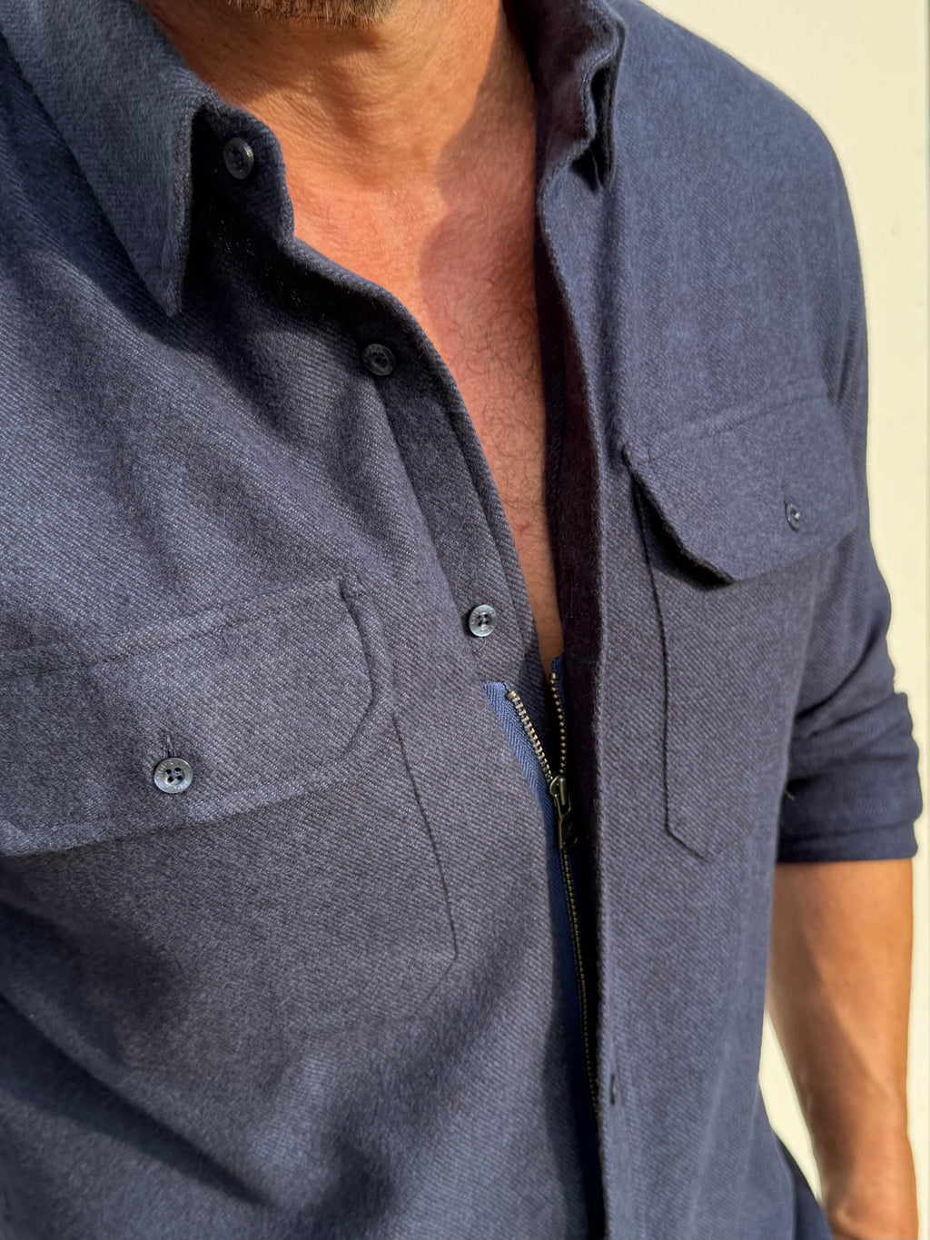 Close-up of a man wearing a dark slate blue button-up shirt with a front zipper and chest pockets.