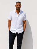 Man wearing a white shirt and black pants against a white wall.
